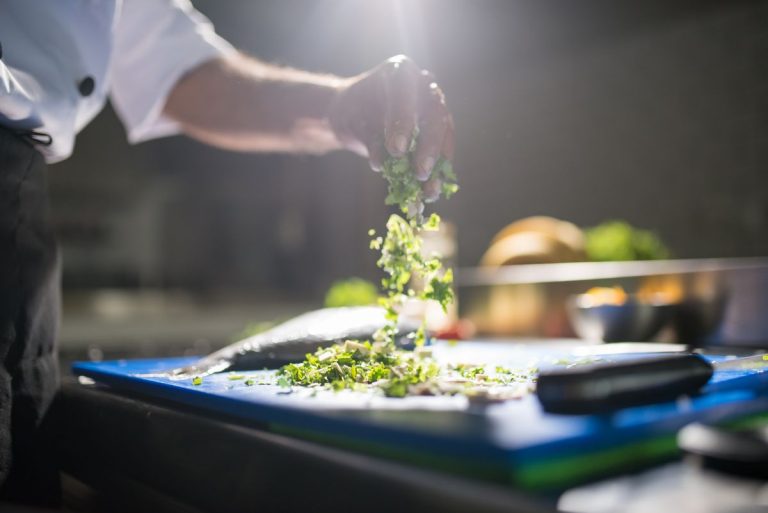 Chef sprinkling fresh herbs over a dish in a restaurant kitchen